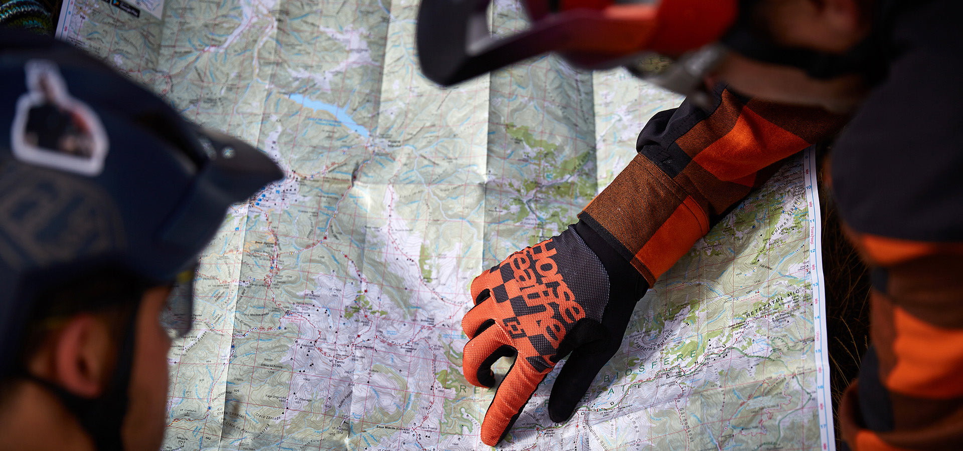 Two people wearing helmets and gloves examine a detailed topographic map, with one person pointing to a specific location near a granite formation.