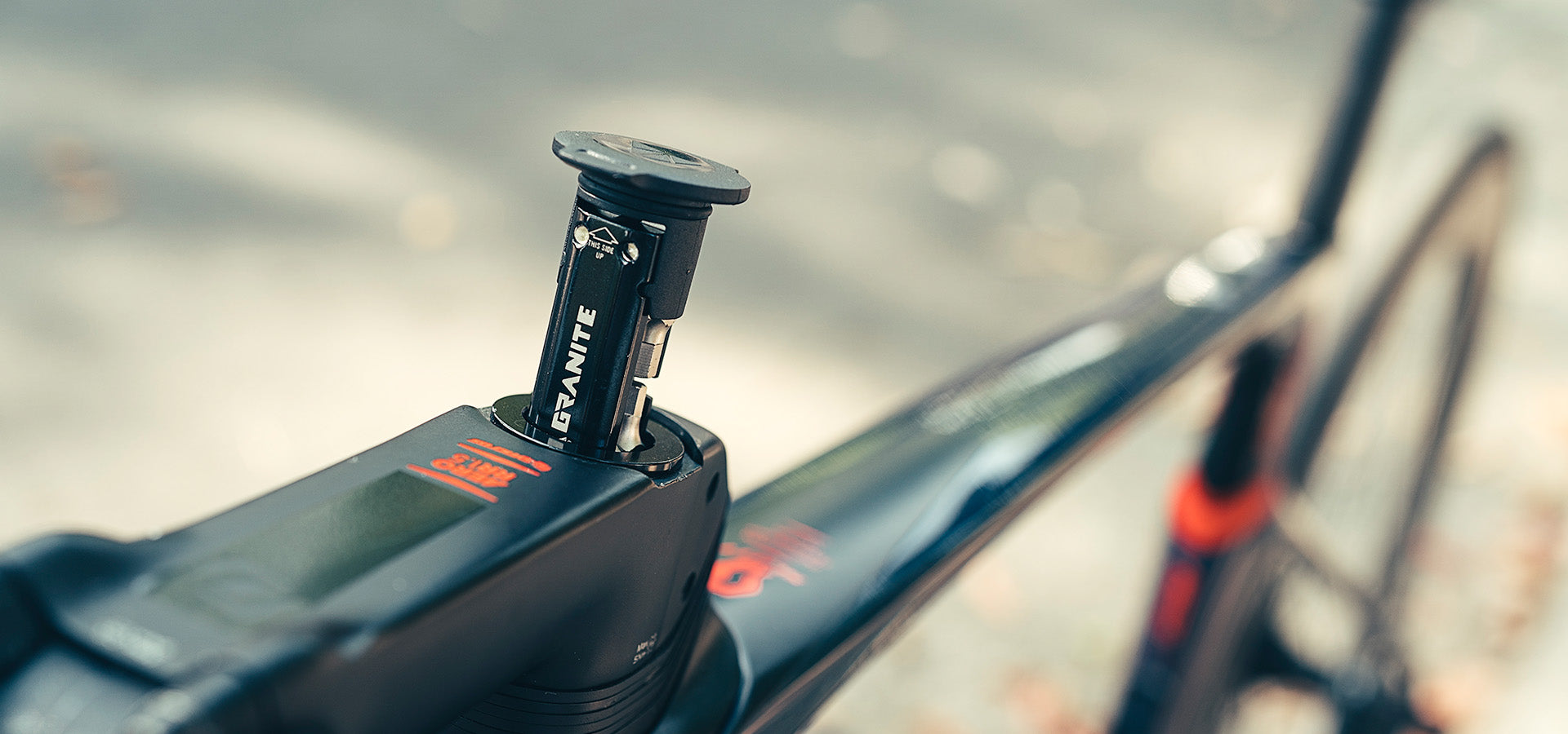 Close-up of a Granite Stash RCX multi tool being inserted into a bike's steerer tube, showcasing the sleek design against a blurred outdoor background.