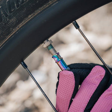 Cyclist wearing purple gloves adjusts a oil slick color Granite valve cap on a bike tire.