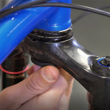 A hand adjusting the cap of Stash Air Tag mount attached to a blue bike frame near the suspension fork.