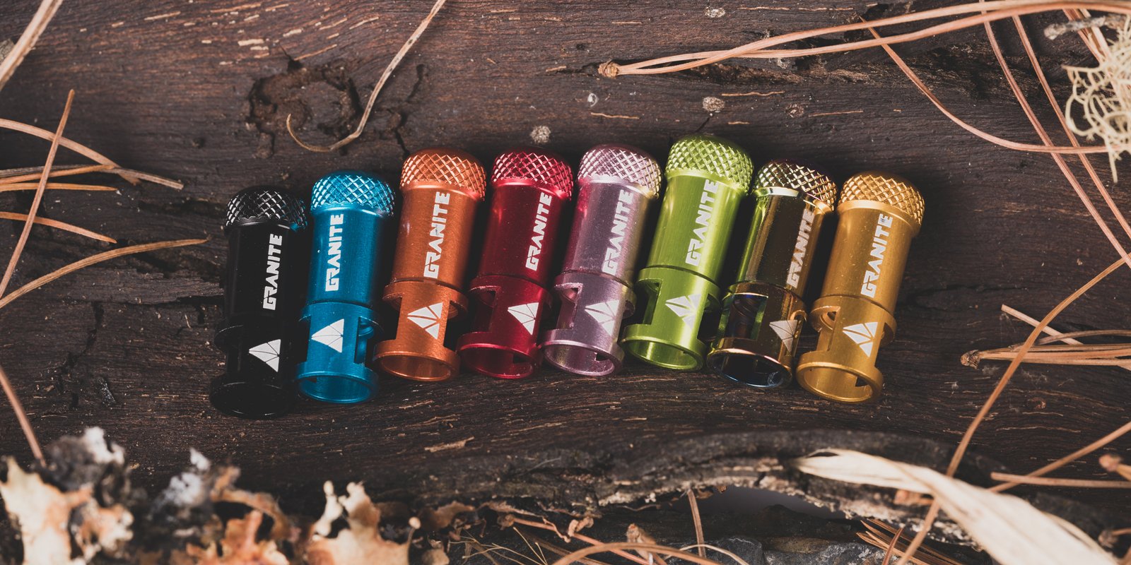 Granite Juicy Nipple valve caps in various colors arranged on a rustic wooden surface.