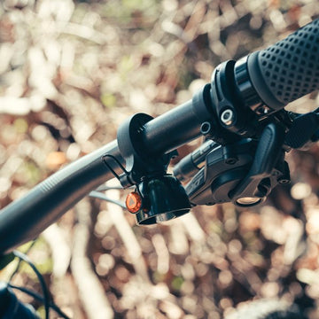 Close-up of a bicycle’s handlebar featuring a Granite black bell and textured rubber grip, set against a blurred natural outdoor background.