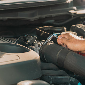 A person’s hand uses a Granite DUET ratchet wrench to tighten a clamp on a black hose under a car hood, performing engine maintenance.