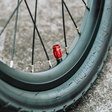 Close-up of a red Granite Juicy Nipple Schrader valve cap on a bike tire, highlighting a sleek and durable design.