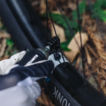 Cyclist using a Granite Punk CO2 inflator to inflate a bike tire on the trail, showcasing quick and efficient tire repair.