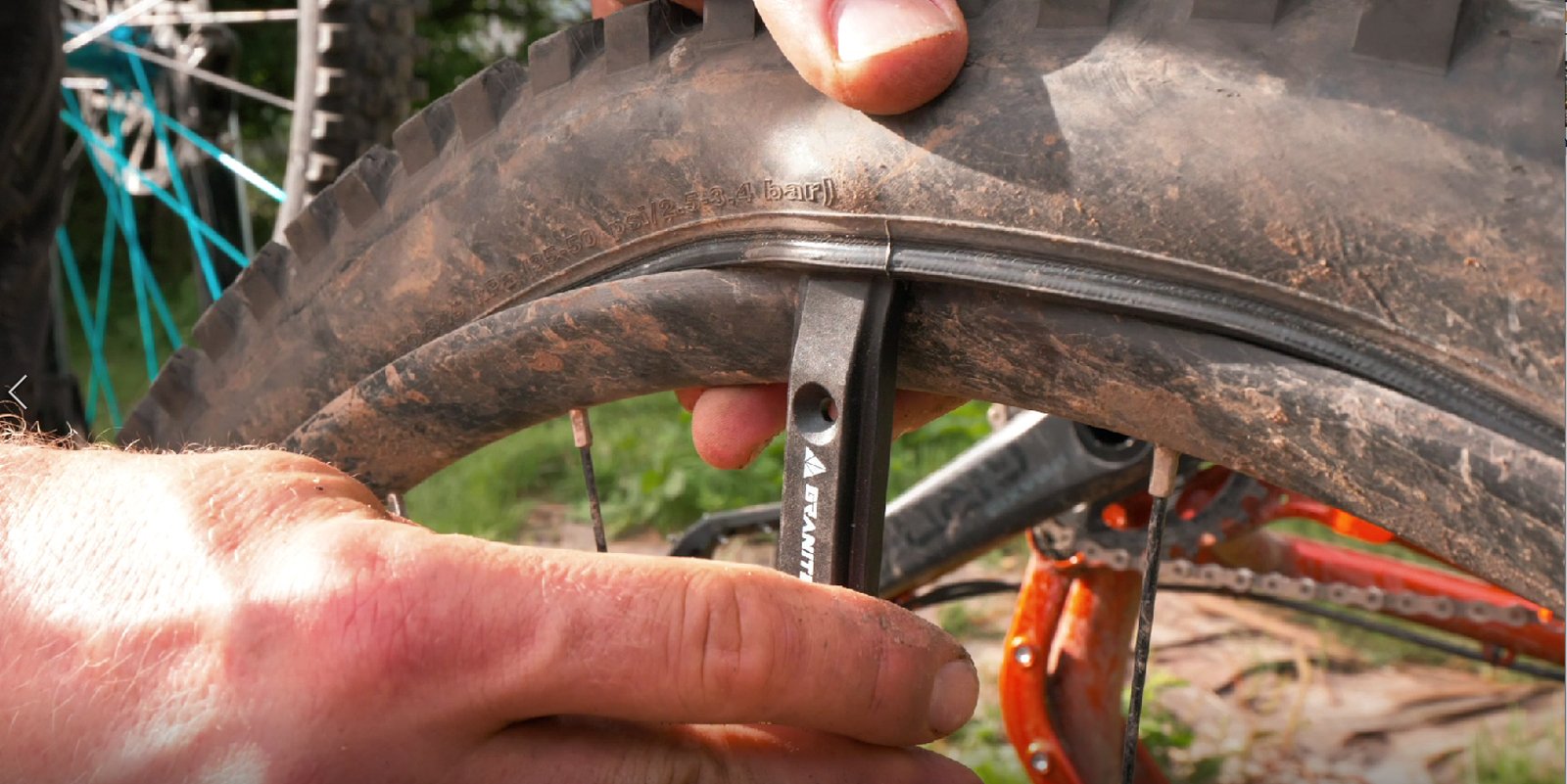 A hand uses a Granite Talon tyre lever to repair a mountain bike tire, with a close-up view of the tire and inner tube.