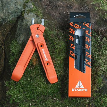An orange Granite tire lever sits beside its packaging on a mossy surface, showcasing its design and branding.