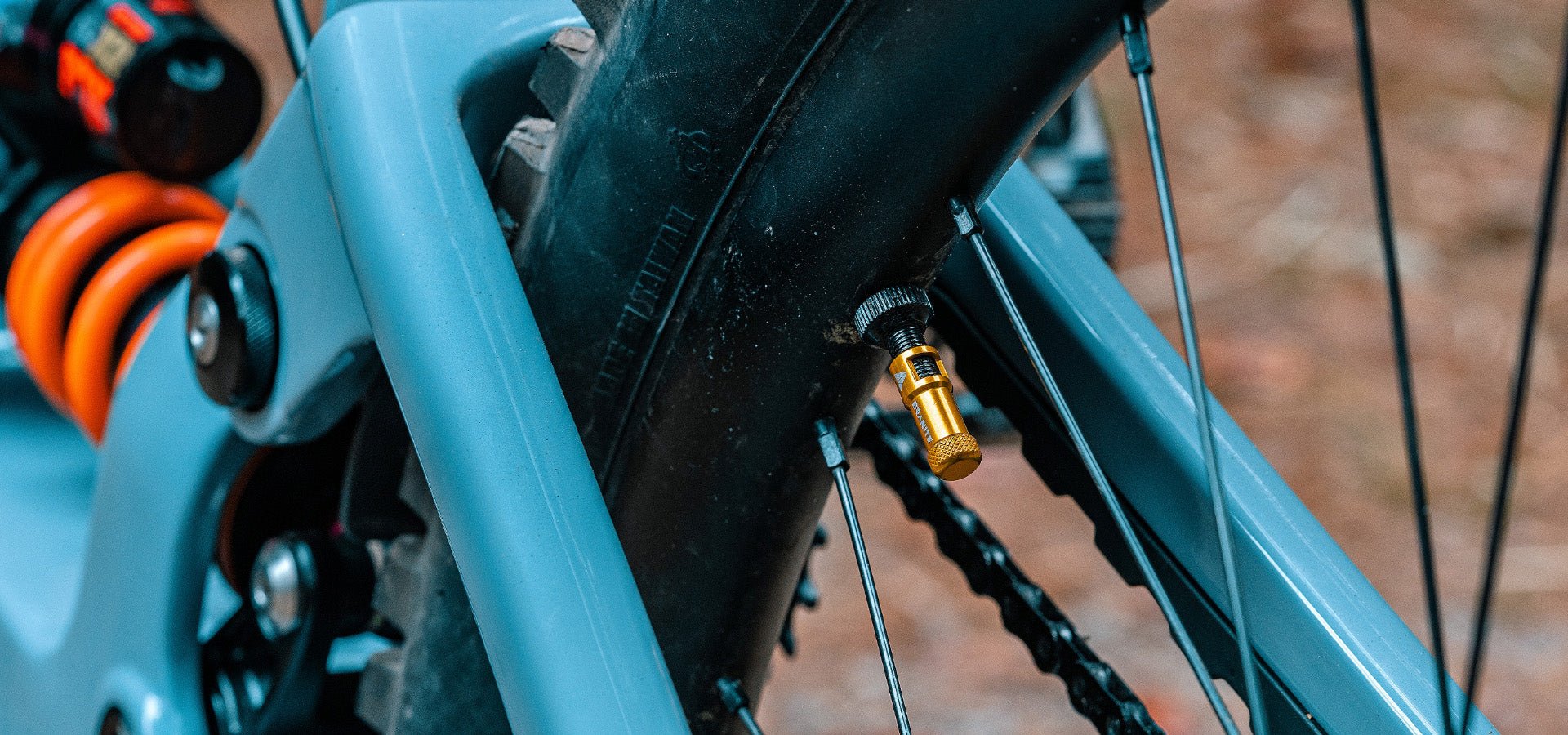 Close-up of a bike's frame with a Granite Juicy Nipple Presta valve cap, anodized in gold, attached to the valve.