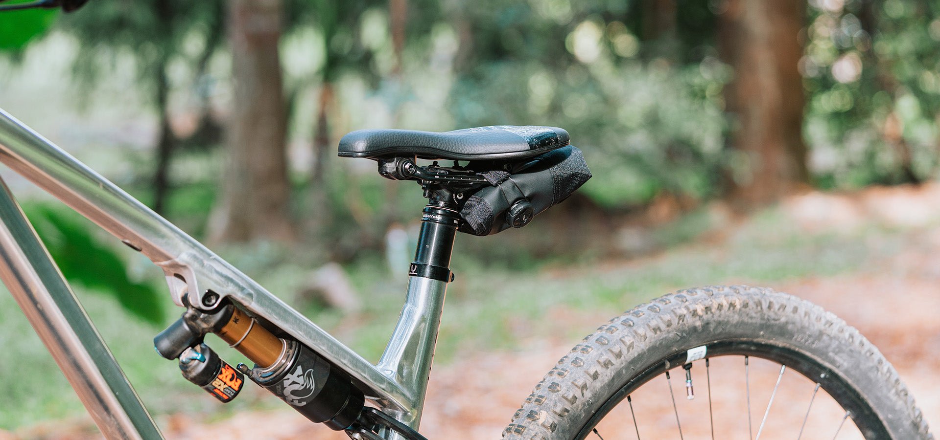 Mountain bike with a Granite Quiver tool roll securely attached under the saddle, surrounded by a forest background.