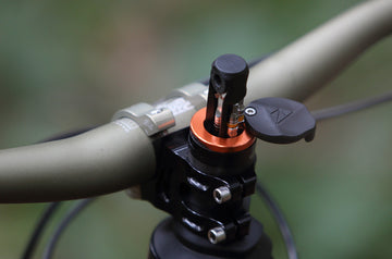 Close-up of a bike's steerer tube showing a Granite Stash RT multi tool inserted, highlighting its vibrant orange color against a blurred background..