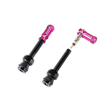 Two black tubeless bike tire valves with pink anodized aluminum Granite valve caps, one assembled and the other with the valve core and cap removed, displayed on a white background.