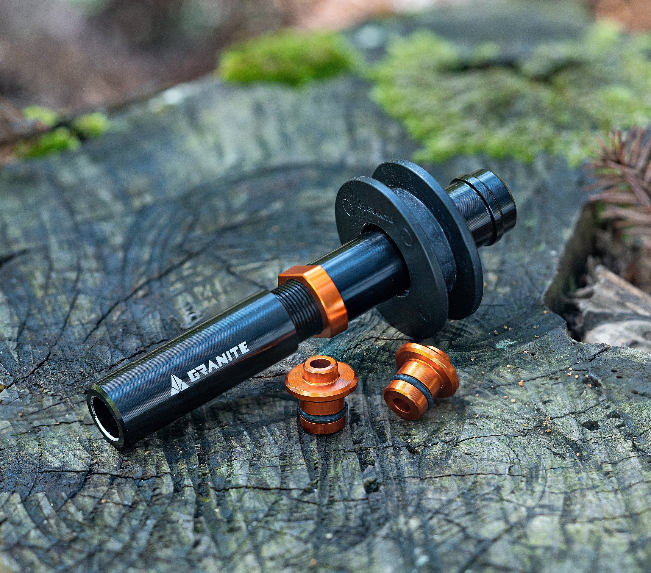 A black and orange bike tool labeled “Granite” rests on a tree stump with two matching small components nearby, surrounded by moss and natural forest elements.