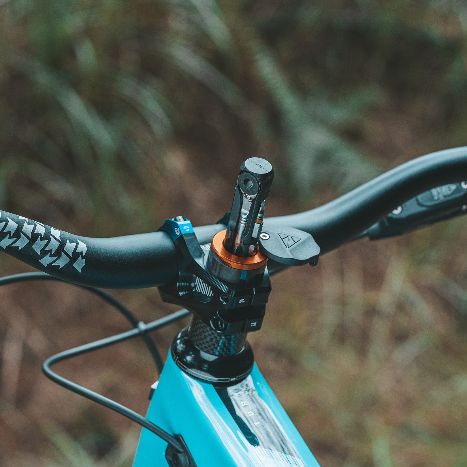 Close-up of a bike handlebar with a Granite Stash RT multi-tool mounted on the steerer tube, showcasing an orange and black design.