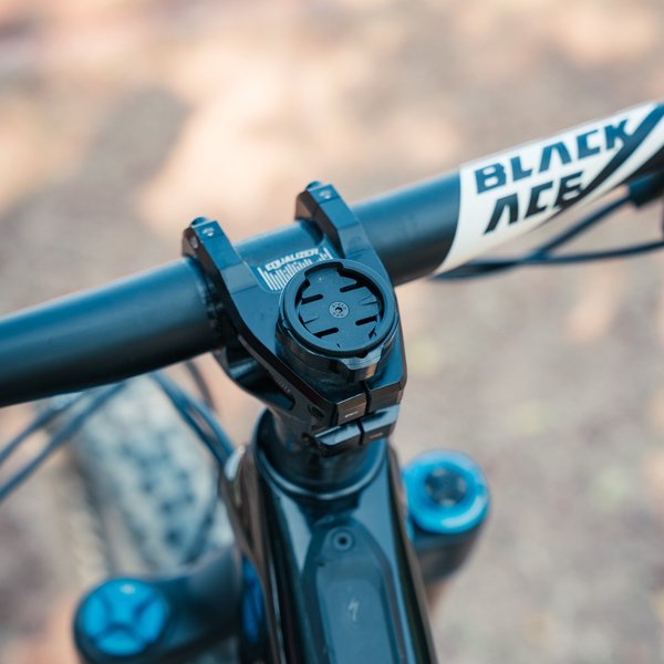 Close-up view of a bicycle’s handlebars with a BLACK ACE logo, featuring a Granite bike computer mount on the stem and parts of the bike’s front fork visible.
