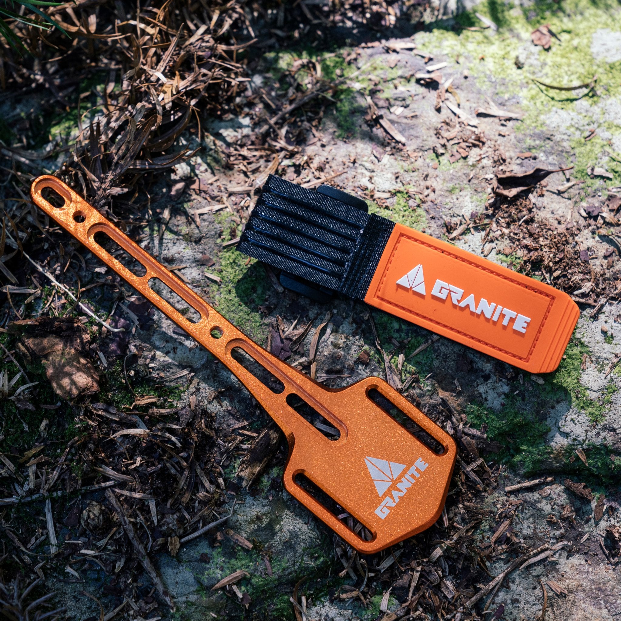 Granite Portaledge XE mounting plate and tool strap displayed on mossy ground, designed for secure attachment to a bike bottle bosses.