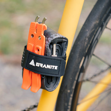 Granite Portaledge strap kit securing orange Talon tire levers and a spare tube to a yellow bike bottle bosses, convenient for on-the-go repairs.