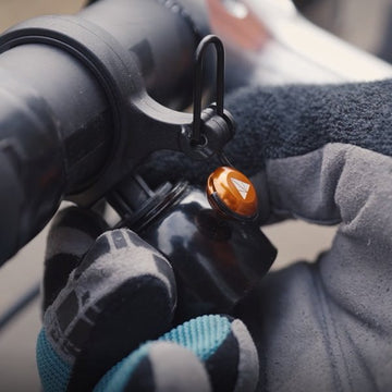 Cyclist wearing gloves adjusts a Cricket bell on a black bike handlebar, featuring a sleek, compact design for easy access.