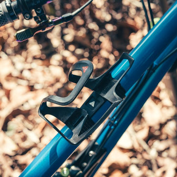 Granite AUX Bottle Cage mounted on a blue bike frame, with a forest floor background.