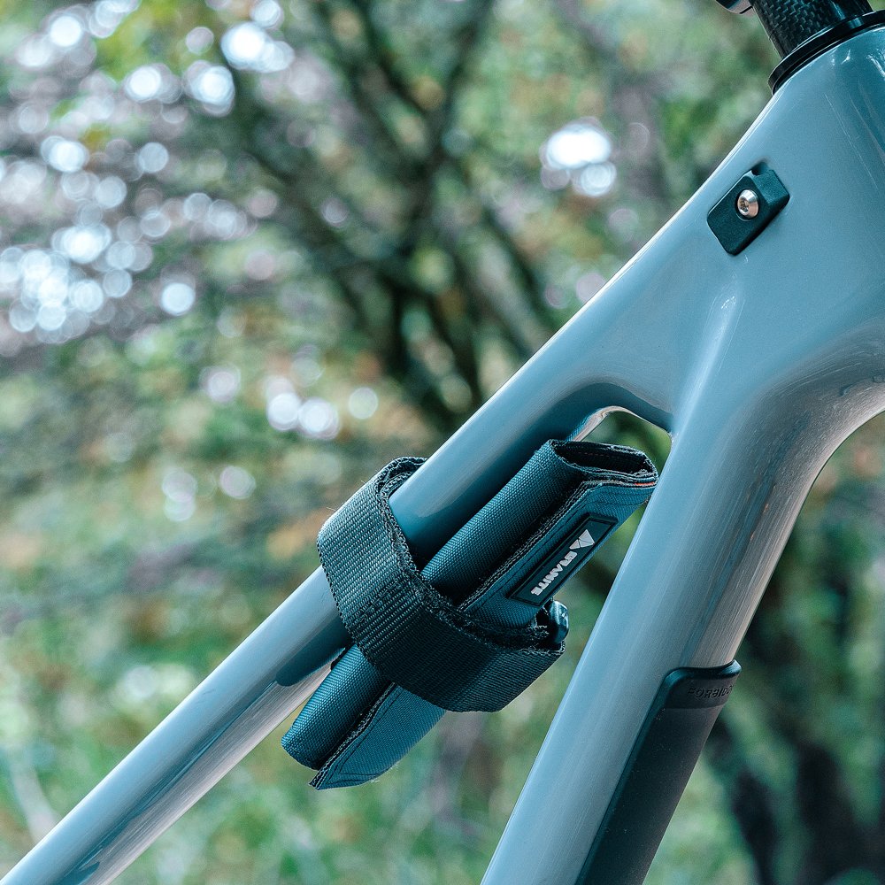 A carrier strap with rocknroll tq tool bag mounted on a blue bike frame, securely holding tools against a natural, blurred background.