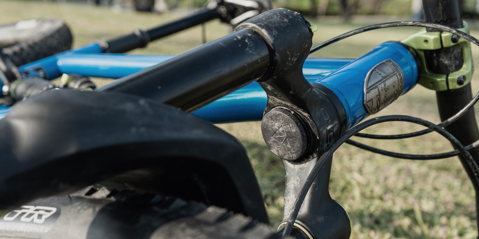 Close-up of a bike frame showing the head tube area with Granite Stash Air Tag Mount and dirt, focusing on details.