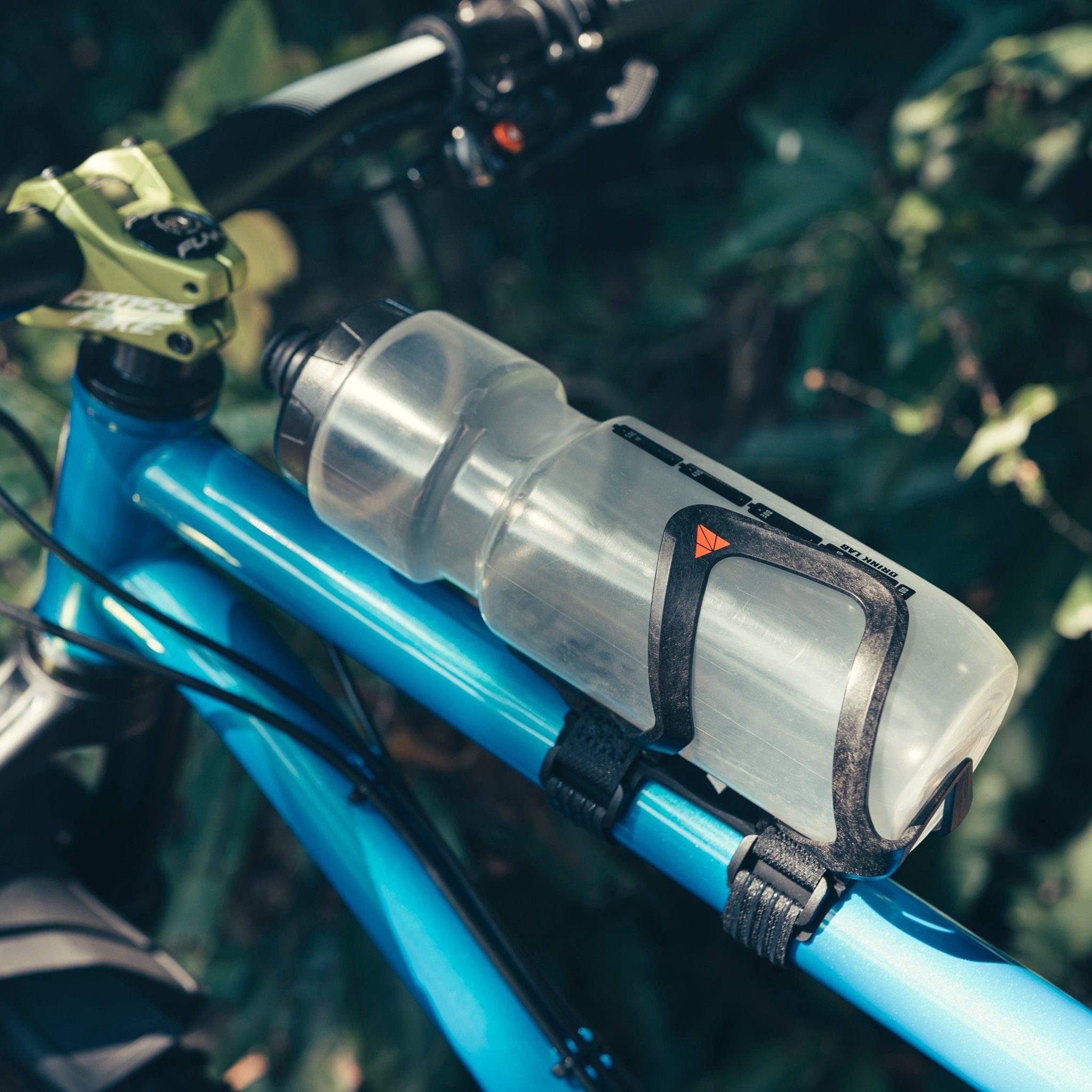 Granite AUX Bottle Cage securely attached to a blue bike frame with a clear water bottle, positioned near the handlebars.