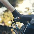 Granite Cricket bike bell mounted on the handlebar near the stem, with white grip tape and background foliage.