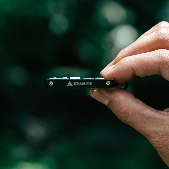 Hand holding a small Granite Diverse 10 multi tool with 'GRANITE' branding against a blurred green background
