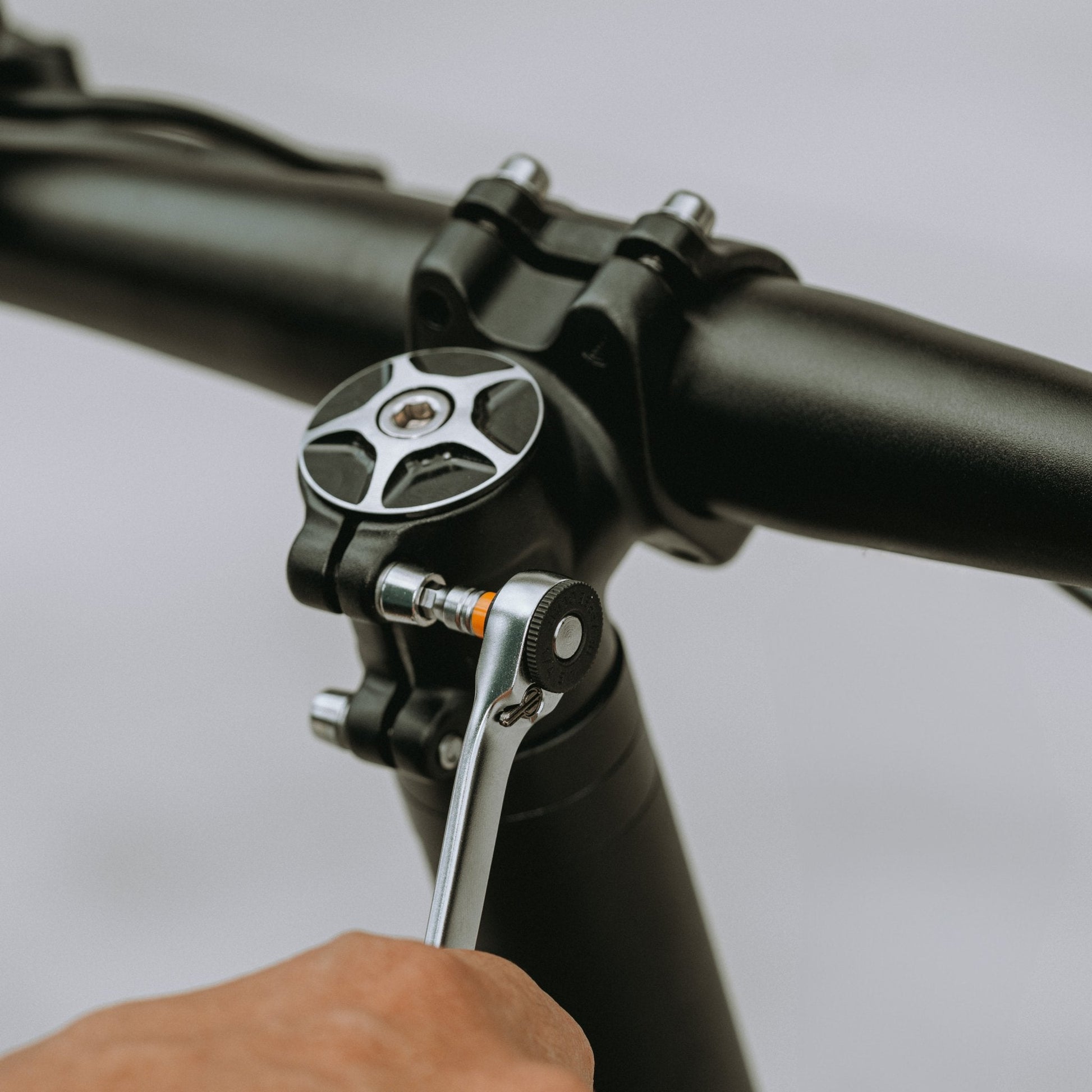 Close-up of a hand using a dual-head ratchet wrench on a bicycle handlebar stem bolt."