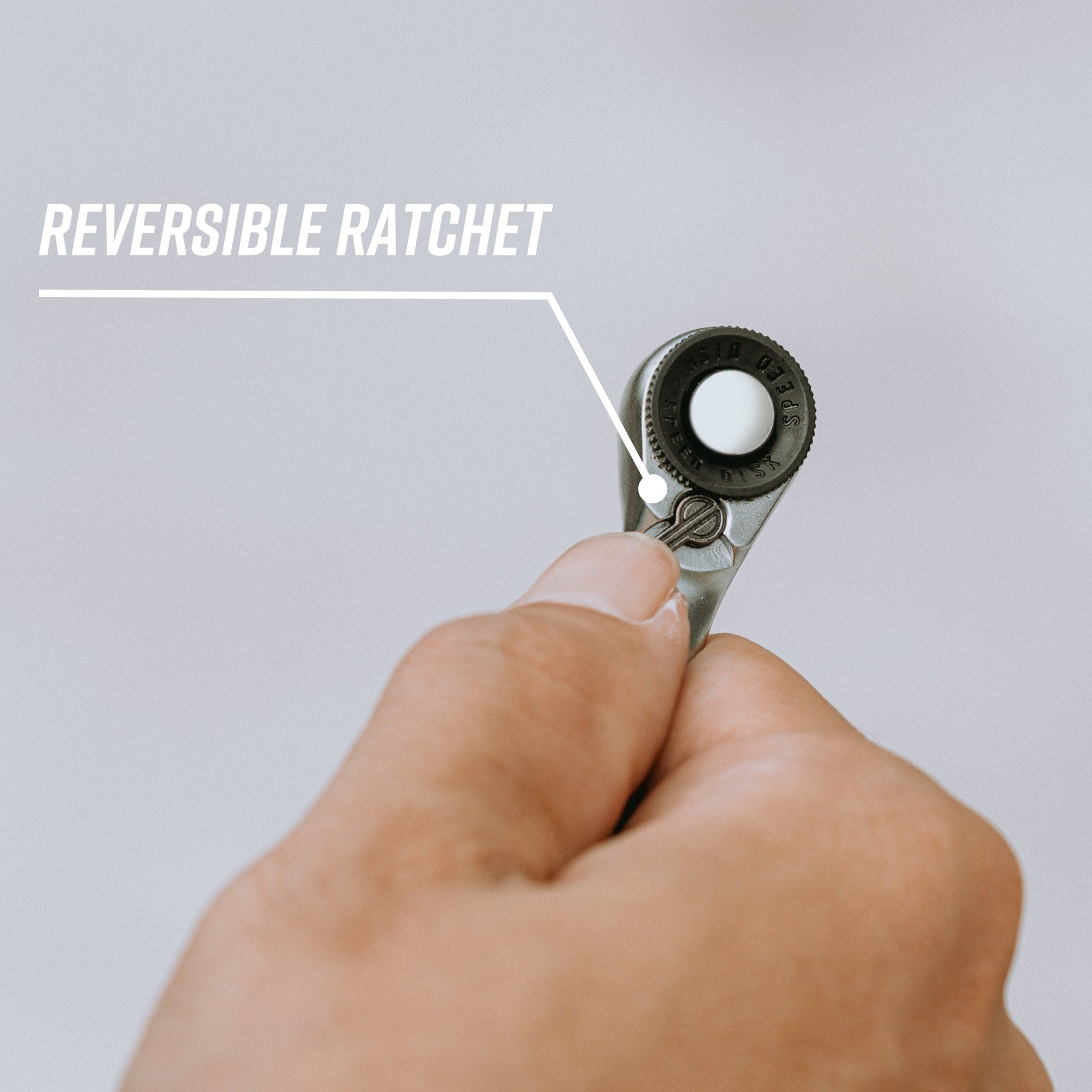 Hand holding a reversible ratchet wrench with a label pointing to the ratchet feature.