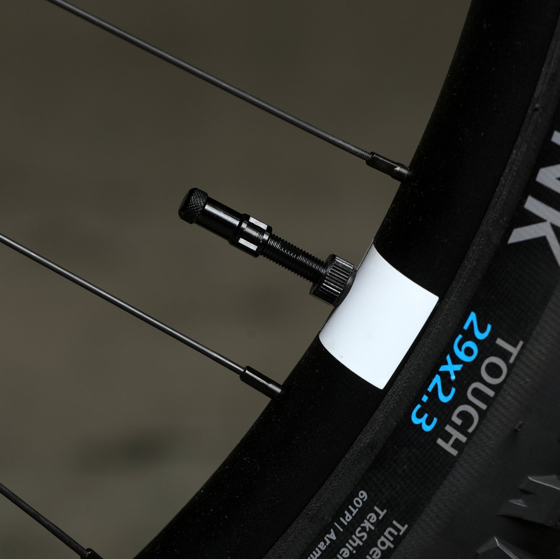 Black Granite Presta valve cap attached to a bike wheel rim, with a close-up of the tread and spokes.