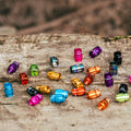 Colorful assortment of anodized Juicy Nipple Schrader Valve Caps scattered on a surface, showcasing colors and textures.