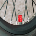 Close-up of a red Juicy Nipple Schrader valve cap on a bike wheel with measurements of 11.6mm width and 17mm height marked.