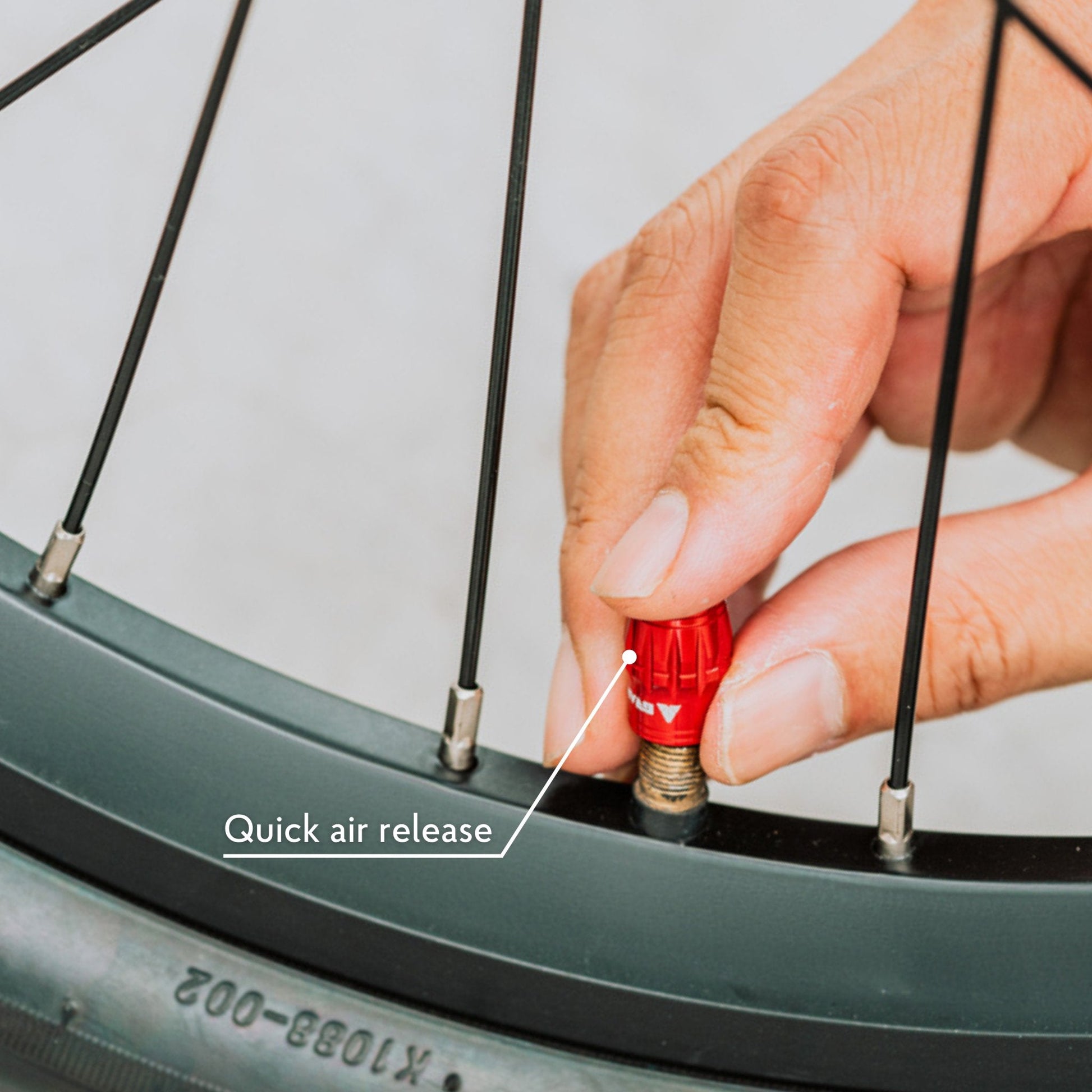 Hand pressing red Juicy Nipple Schrader valve cap on bike wheel for quick air release, labeled for easy inflation control.