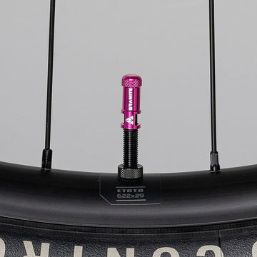 Granite Juicy Nipples pink alloy Presta valve core remover cap mounted on a black bicycle rim for easy tubeless tire service