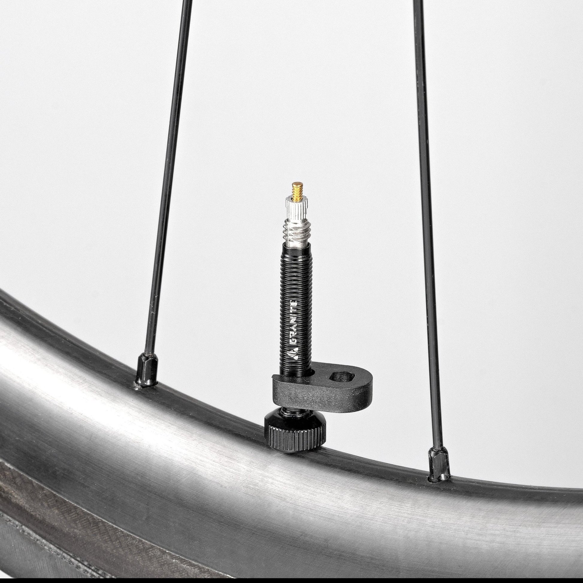 Granite Presta valve stem extender on a bike rim with a removal tool attached.