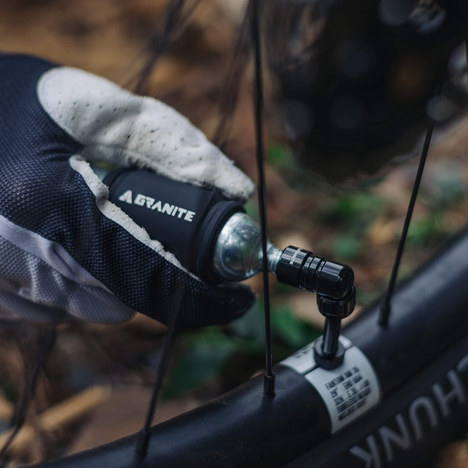 Gloved hand using a Punk CO2 inflator on a bike tire, with the inflator securely attached to the valve for quick inflation.