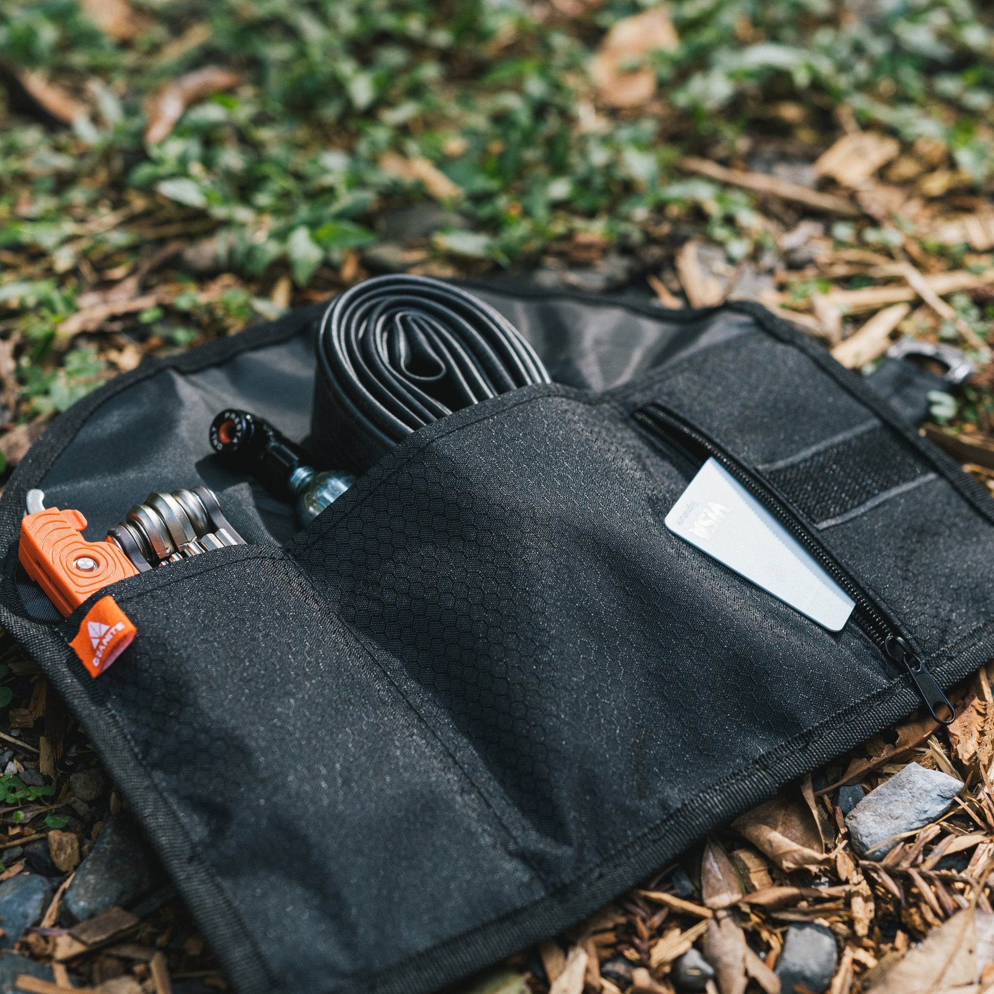 Quiver Tool Roll opened on the ground, displaying organized compartments with tools, tube, and repair essentials for biking.