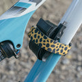 Leopard print Granite Rockband Plus frame strap securing a spare inner tube and tire lever to a blue and white bike frame.