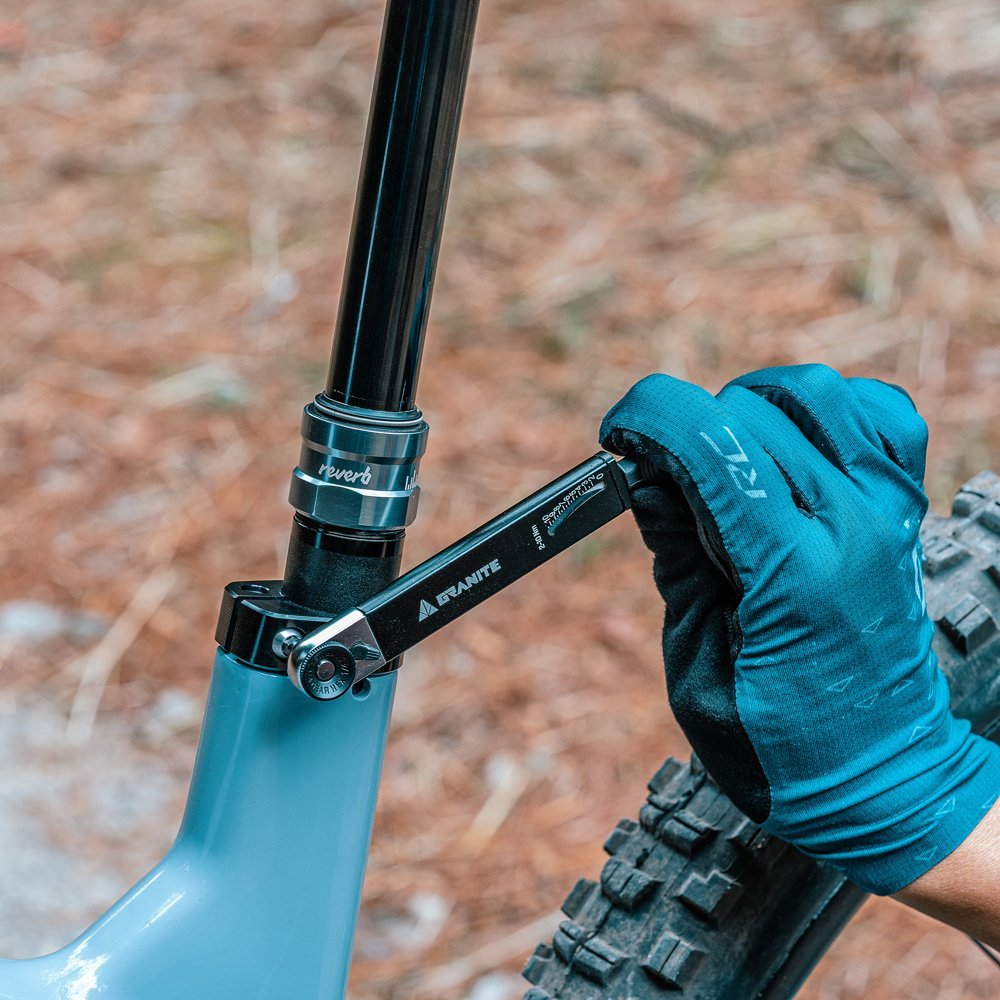 Gloved hand using Granite TQ torque wrench on bike seat post for precise adjustments.