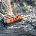 Granite Stash Chain Repair Tool in Orange resting on a tree branch, showcasing its compact and rugged build for outdoor use.