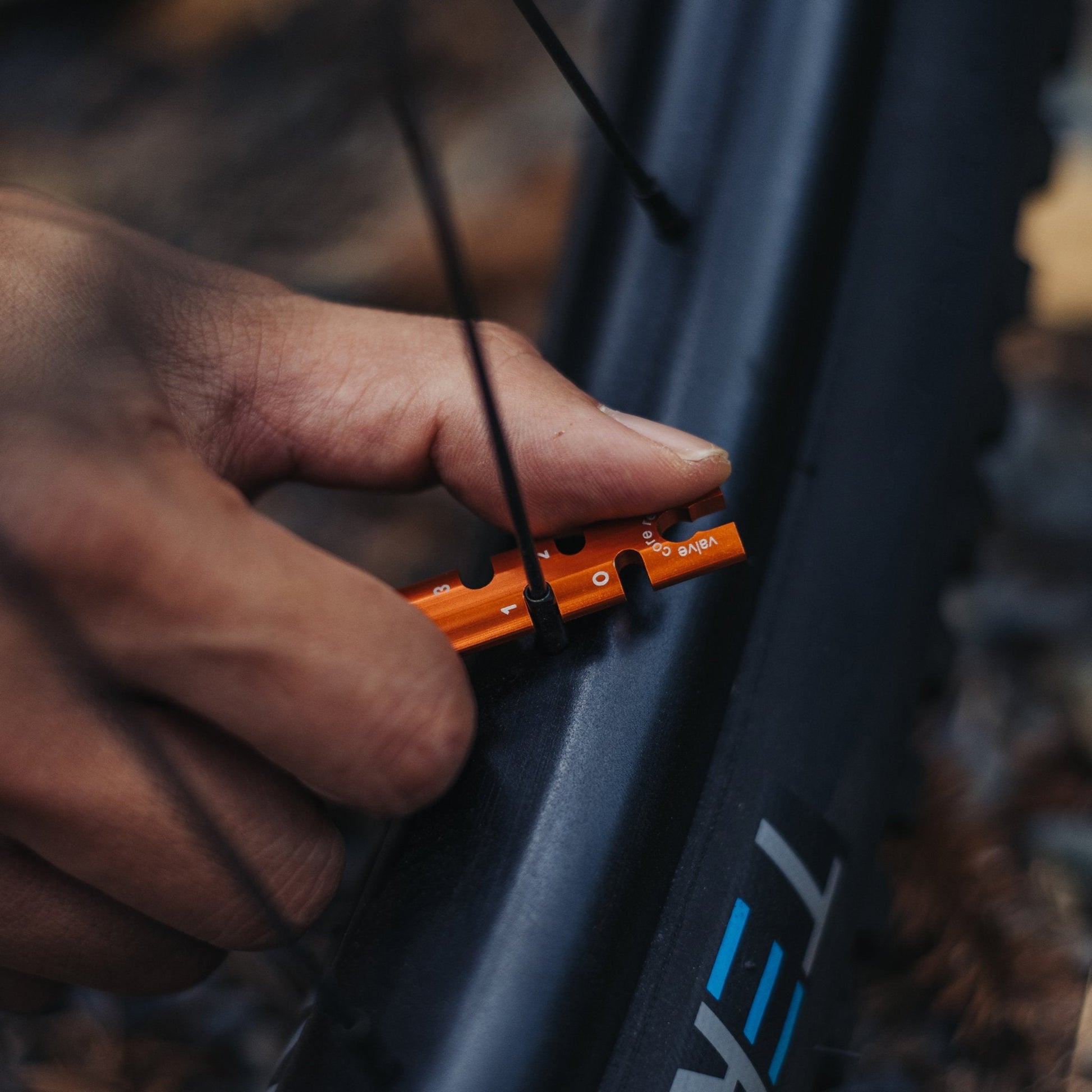 Close-up of a hand using an orange Granite spoke tension tool on a bike wheel.