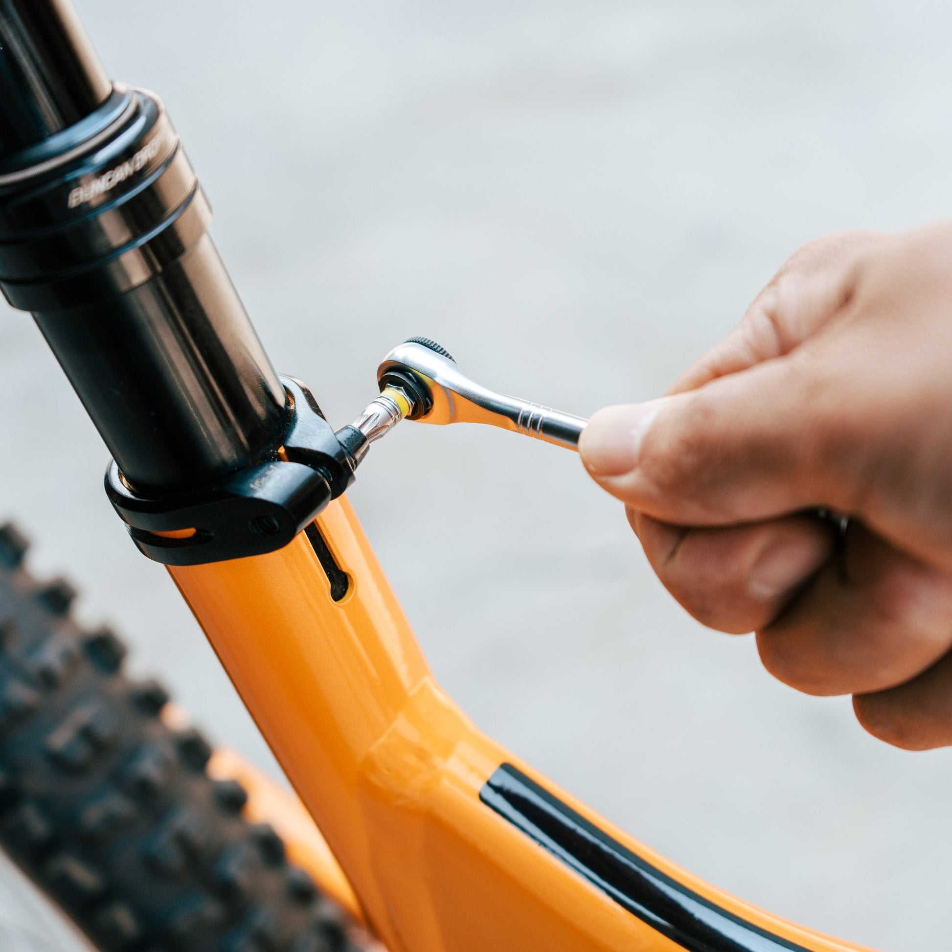 Close-up of a hand using a ratchet tool to adjust a bike's dropper post clamp on an yellow bike frame.