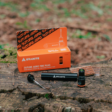 Granite Suture Aero Tire Plug Kit with black aluminum tubeless repair tool and plugs on tree stump, orange branded packaging behind