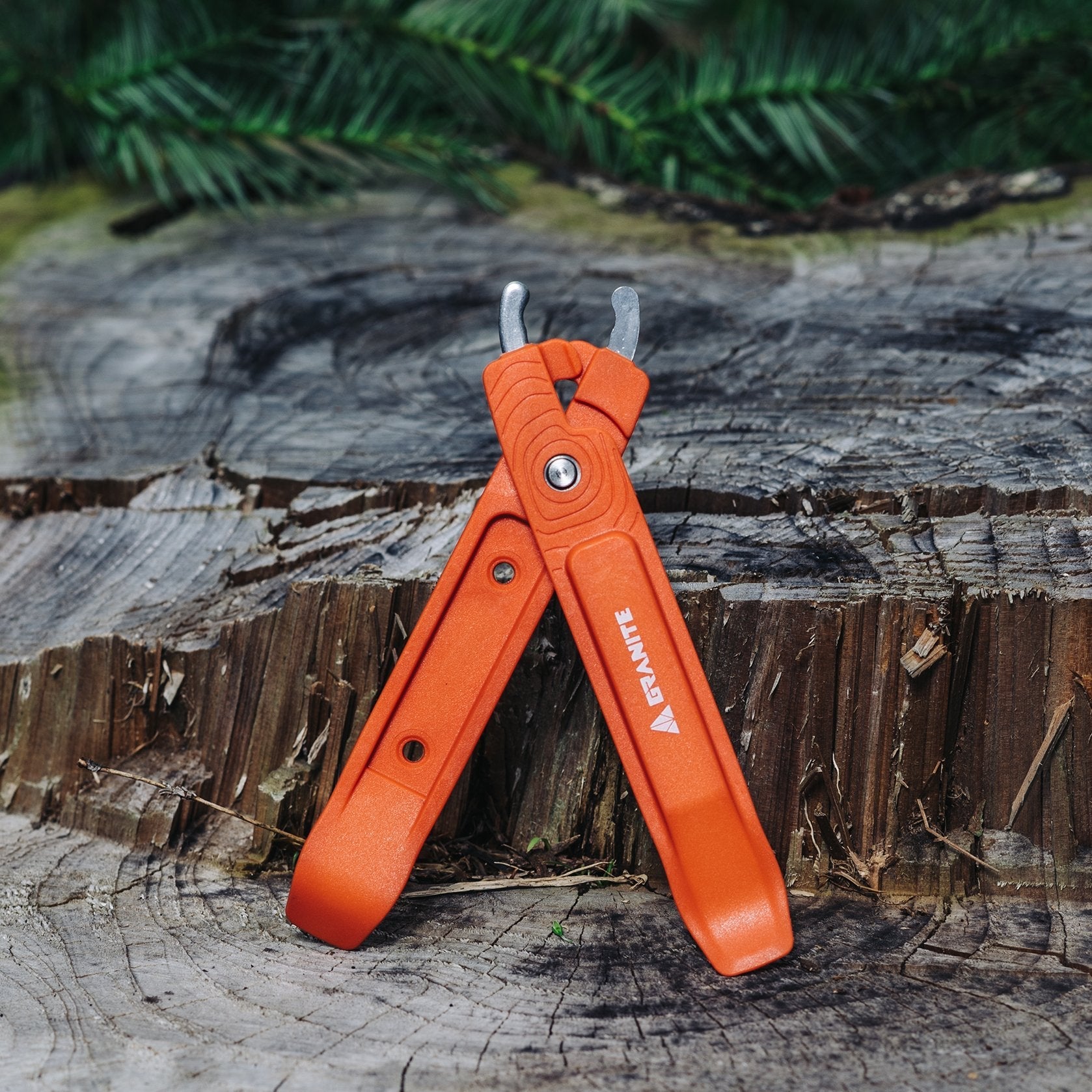 Orange Talon bike tire levers with built-in master link pliers, displayed on a rustic tree stump with greenery.