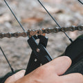 Close-up of a hand using a Talon master link plier to open a quick link on a bike chain, with a blurred outdoor background.