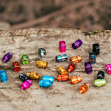 Juicy Nipple Schrader valve caps in many colors scattered on a weathered log