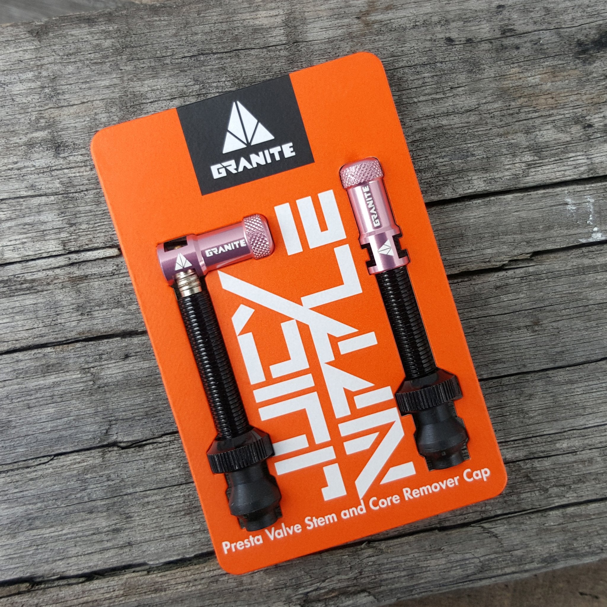 Granite Juicy Nipple Presta Valve Stem and Core Remover Cap in pink, packaged on an orange display card on rustic wood.