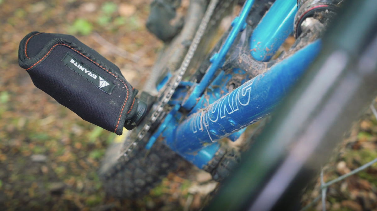 PITA black neoprene crank protector on blue mountain bike, padded cover shielding pedal arm from trail impact and scratches