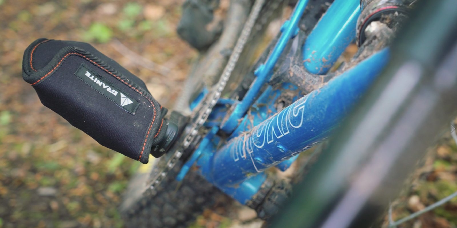 Granite Pita Pedal Cover in black with orange stitching attached to a blue bike pedal, providing protection during transport.