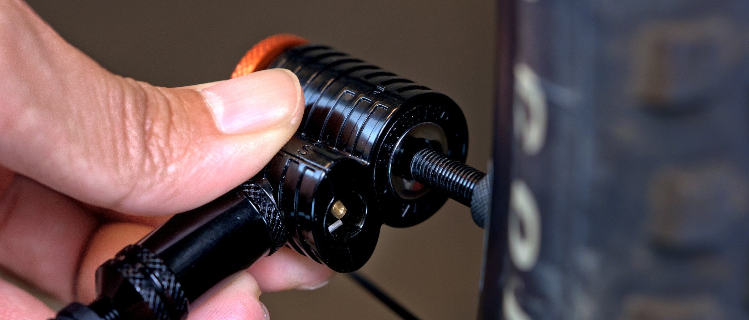 Hand pushing a black Granite Quickie pump head with orange cap straight onto the valve of a gravel bike tire